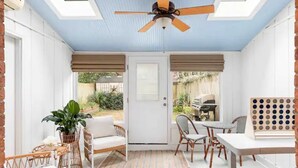 Ein Wintergarten mit Deckenventilator, Korbmöbeln und Blick auf den Garten.