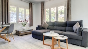A modern living room with a grey sofa, a round coffee table, and a dining area with a table and chairs. - Villa with private pool, close to the beach (El Carmoli)