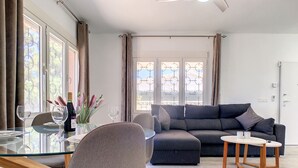 A modern living room with a glass dining table, grey sofa, and a small side table. - Villa with private pool, close to the beach (El Carmoli)