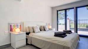 A bedroom with a bed, bedside tables, a ceiling fan, and a large window with a view of greenery. - Villa with private pool, close to the beach (El Carmoli)