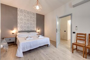 Quarto com cama grande, mesas de cabeceira, luminária pendente e porta para outro cômodo.