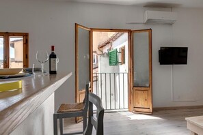 Uma cozinha com bancada de madeira, uma cadeira, uma garrafa de vinho e uma televisão na parede.