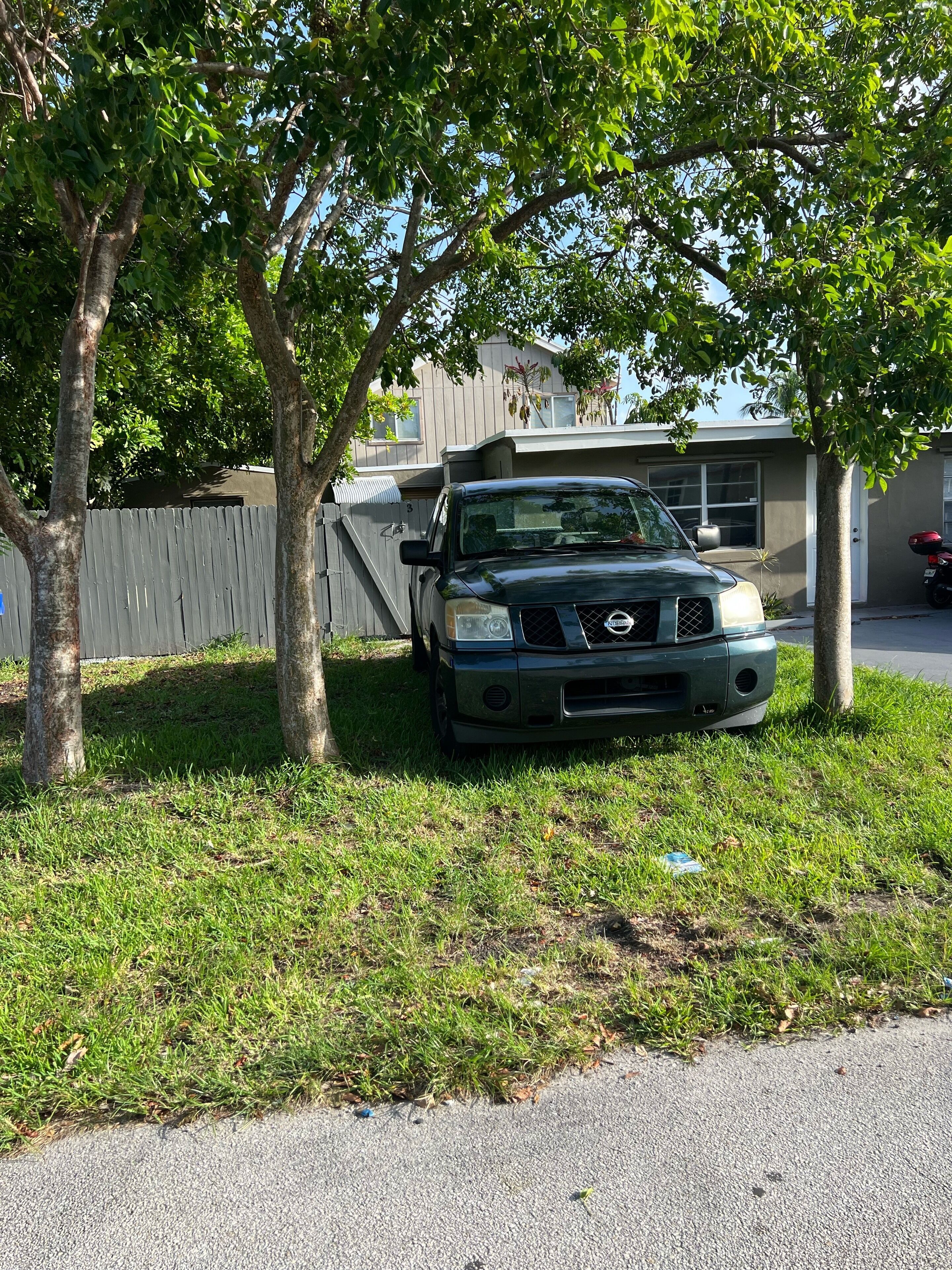 Un vehículo estacionado en un área cubierta de césped, con árboles y una casa al fondo.