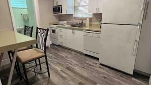 Une cuisine compacte avec des meubles blancs, un four à micro-ondes, un réfrigérateur et un coin repas comprenant une table et des chaises.