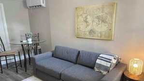 Un salon avec un canapé gris, une petite table ronde et une œuvre d’art représentant une carte accrochée au mur.