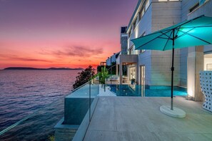A modern hotel with a glass infinity pool overlooking the sea, a private outdoor seating area, and a view of the sunset. - Adriatic Beach House (Vrbica)
