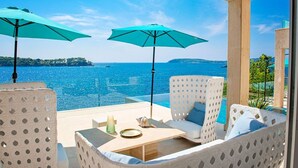 A terrace with white wicker furniture, two turquoise umbrellas, and a view of the sea. - Adriatic Beach House (Vrbica)