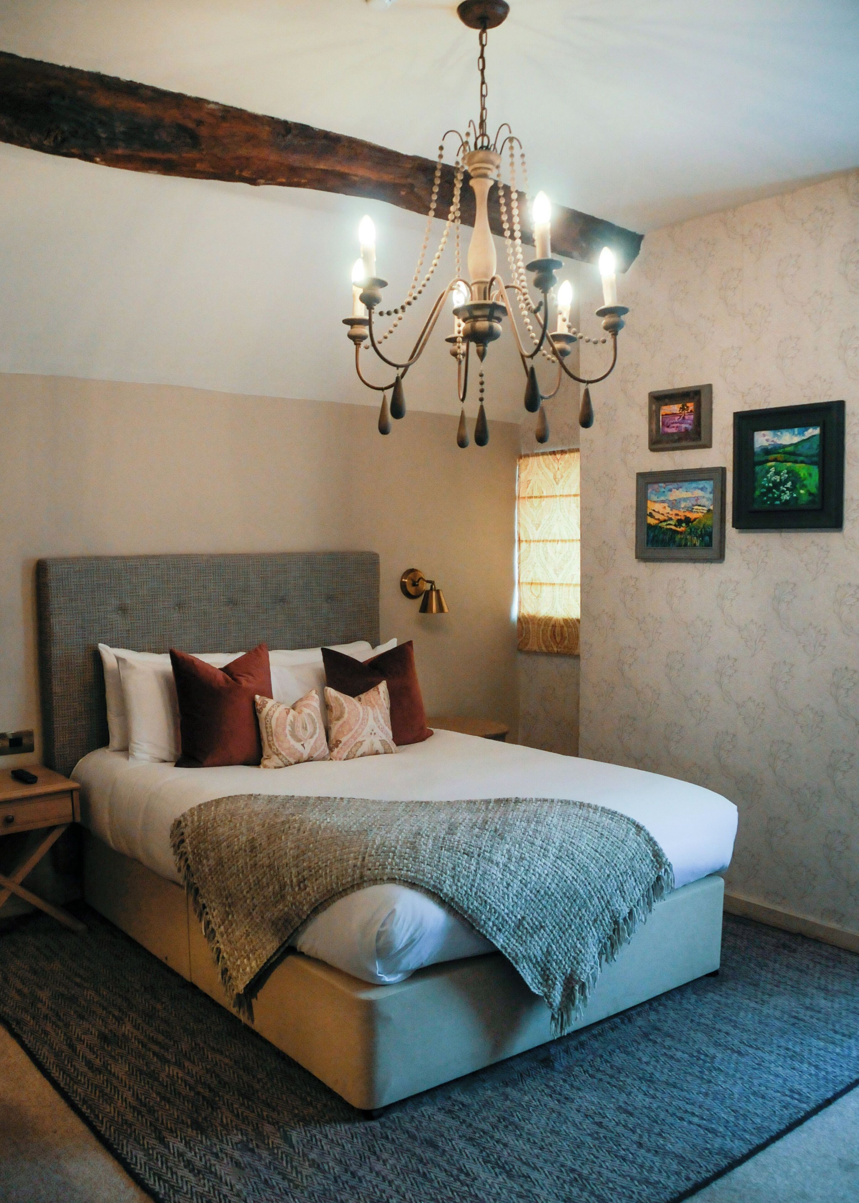 A bedroom with a bed, a chandelier, a nightstand, a wall clock, and framed pictures.