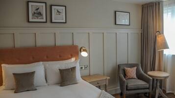 Een hotelkamer met een bed, een stoel, een klein tafeltje en wanddecoraties in lijsten.