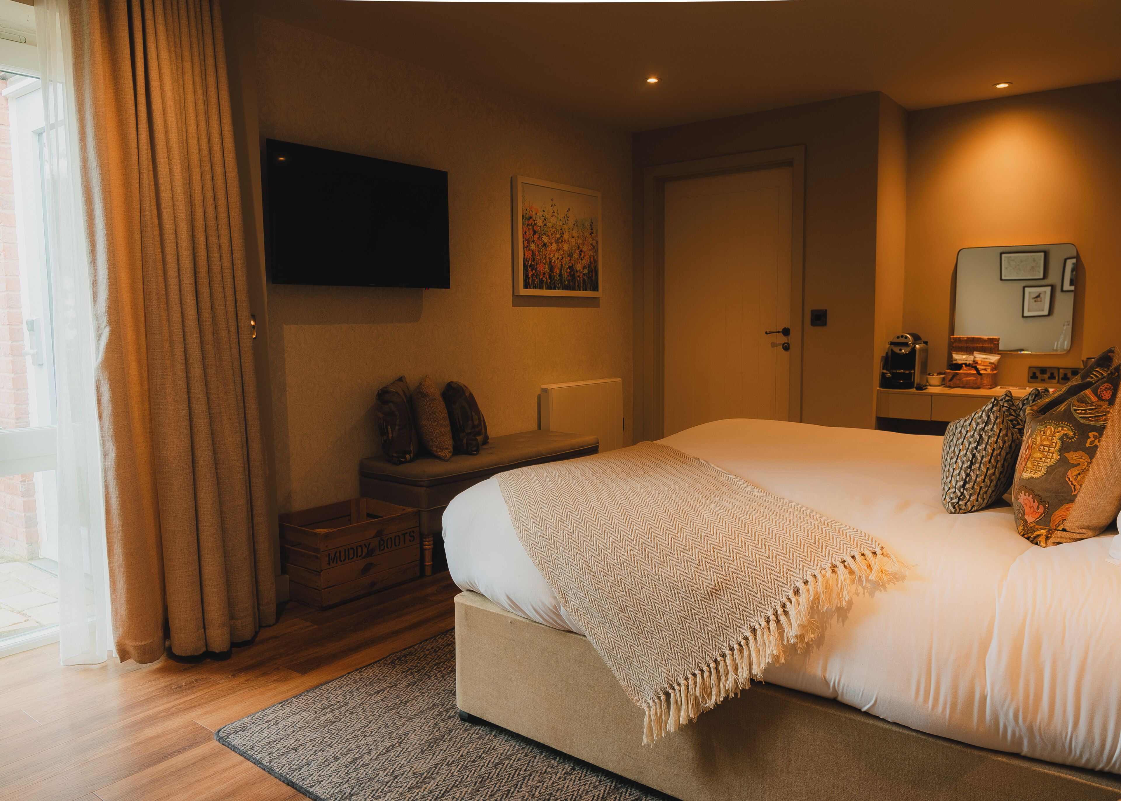 A bedroom with a bed, a television on the wall, a suitcase, and a window with curtains.