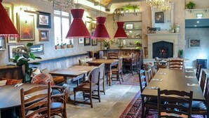A restaurant with wooden tables and chairs, red pendant lights, and a fireplace. - The Lion at Malpas (Malpas)