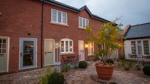 A brick building with multiple doors and windows, a paved courtyard with a large planter, and outdoor seating. - The Lion at Malpas (Malpas)