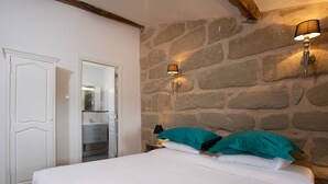 Ein Schlafzimmer mit einer Steinwand, einem Bett mit weißer Bettwäsche, türkisfarbenen Kissen und zwei Wandleuchten.