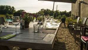 Ein Essbereich im Freien mit einem Holztisch, Stühlen und einem großen Sonnenschirm.