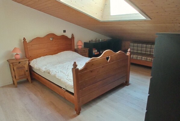 A bedroom with a wooden bed, a nightstand, a lamp, and a bench.