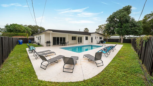Un giardino con piscina, lettini da relax e una zona patio coperta.