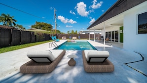 Un giardino sul retro con piscina, sedie a sdraio e zona pranzo.