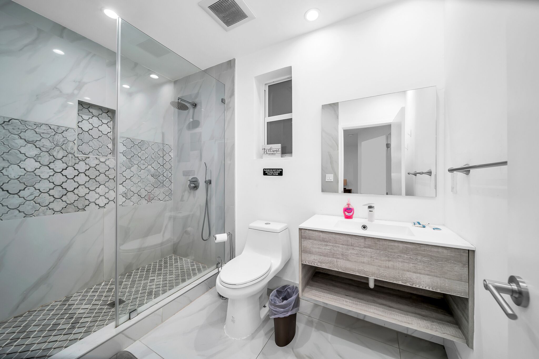 A modern bathroom with a glass-enclosed shower, a toilet, and a sink with a mirror above it.