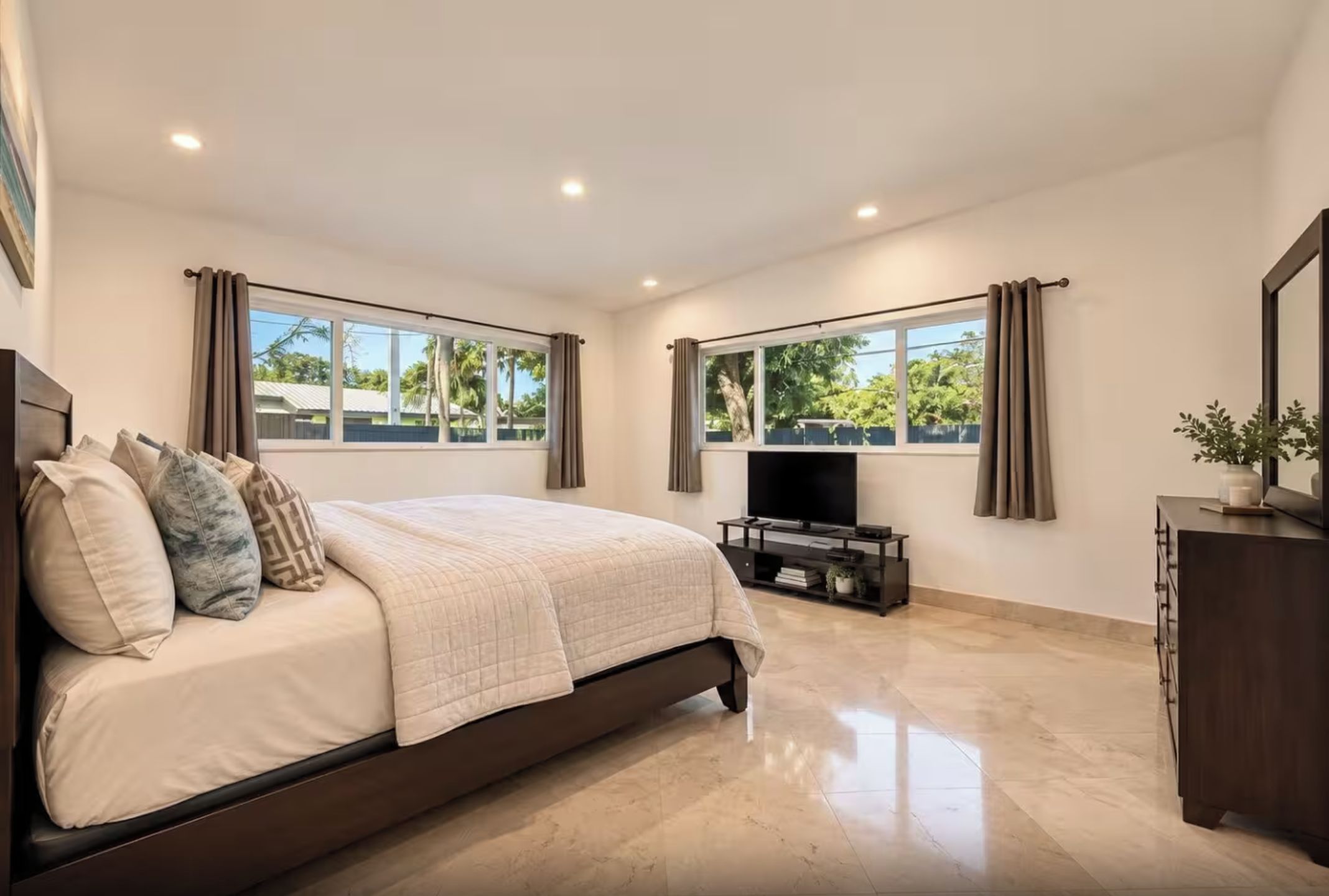 A bedroom with a bed, a TV, a dresser, and windows with curtains.