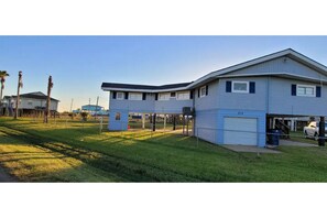 A two-story building with a garage, a covered parking area, and a grassy lawn. - Sun Crest Villa, NEWLY REMODELED!! (Surfside Beach)