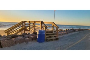 A wooden staircase leading to a beach area with a blue barrel and a flagpole. - Sun Crest Villa, NEWLY REMODELED!! (Surfside Beach)