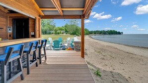 Eine Holzterrasse mit blauen Stühlen und einem Tisch, mit Blick auf einen Strand und Wasser.