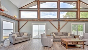 Ein geräumiges Wohnzimmer mit hoher Decke, großen Fenstern und Blick ins Freie.