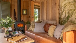 Une pièce chaleureuse avec un décor intérieur en bois, un canapé en cuir, une table avec une bougie et un livre, et un poêle à bois.