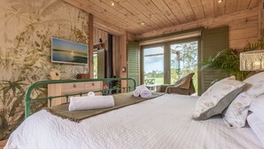 Une chambre à coucher avec un lit, une tête de lit en métal verte, un tableau, une fenêtre et une plante.