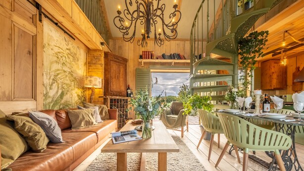 Un salon spacieux avec un canapé en cuir, une table basse en bois et un coin repas comprenant une table et des chaises en métal vert.