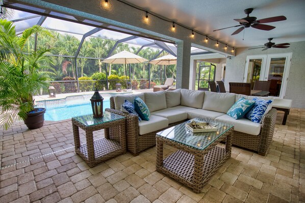 A covered outdoor seating area with a pool, wicker furniture, and umbrellas.