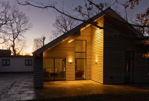 A modern house with a sloped roof, large glass doors, and a patio area. - Missy's House in the Woods - Harringworth , Northamptonshire (Harringworth)