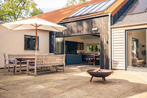 A patio with a wooden bench, a table, and an umbrella. - Missy's House in the Woods - Harringworth , Northamptonshire (Harringworth)