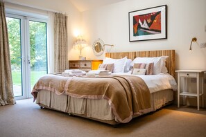 A bedroom with a large bed, a bedside table, a lamp, a mirror, and a painting on the wall. - Missy's House in the Woods - Harringworth , Northamptonshire (Harringworth)