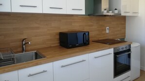 Una cocina moderna con armarios blancos, encimera de madera, microondas integrado, un fregadero y un horno.