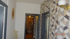 Un pasillo con papel tapiz estampado, una puerta que da a una habitación y una lámpara fijada a la pared.