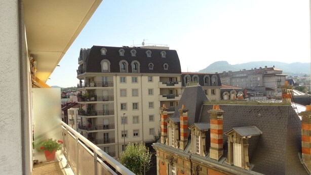 Un balcón con vistas a un edificio de varios pisos con un estilo arquitectónico particular, que incluye una chimenea destacada y un balcón con macetas.