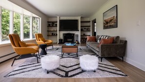 A modern living room with a fireplace, comfortable seating, and a large window. - Birch Hill - Luxury Mountain Retreat (Windham)