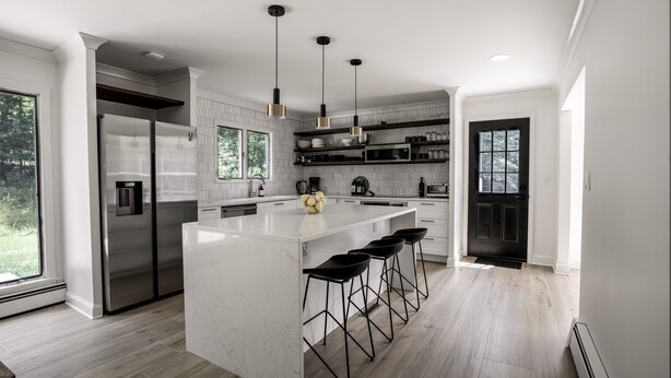 A modern kitchen with a large island, stainless steel appliances, black bar stools, and pendant lighting. - Birch Hill - Luxury Mountain Retreat (Windham)