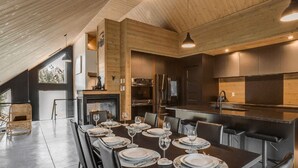 A modern kitchen with stainless steel appliances, a dining area with a long table set for six, and a high ceiling with wooden beams. - The Experience SÔ Lodge (SHEFFORD)