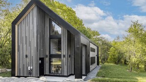 A modern, wooden cabin with a large glass door and windows, surrounded by trees and a clear sky. - The Experience SÔ Lodge (SHEFFORD)