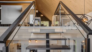 A modern interior with a staircase leading to an upper level, featuring a wooden ceiling and glass railings. - The Experience SÔ Lodge (SHEFFORD)