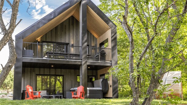 A modern cabin with a large deck, outdoor seating, and a natural setting. - The Experience SÔ Lodge (SHEFFORD)