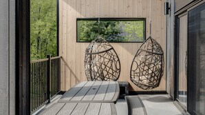 Une terrasse en bois avec deux fauteuils suspendus et une table.