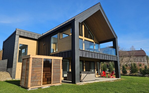 A modern two-story house with large windows, a balcony, and a wooden deck.