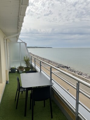 Eine Terrasse mit Tisch und Stühlen mit Blick auf einen Strand mit felsigem Ufer und einer entfernten Insel.