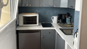Une cuisine compacte avec des meubles gris, un micro-ondes blanc, un évier et un luminaire suspendu jaune.