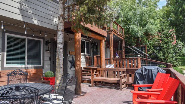 Una terraza de madera con mobiliario exterior, que incluye una mesa, sillas y un banco.