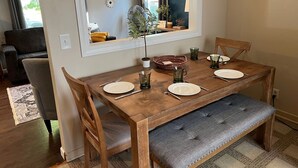 A dining area with a wooden table, four chairs, a bench, and a clock on the wall.