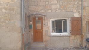 Un edificio de piedra con puerta de madera, una ventana con contraventanas y un pequeño porche.